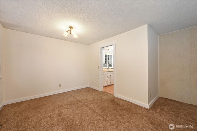 spare room featuring a textured ceiling, baseboards, and light carpet