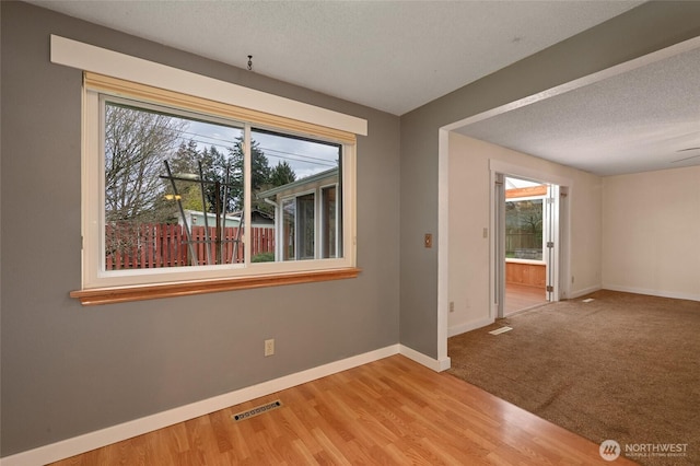 empty room featuring plenty of natural light, visible vents, a textured ceiling, and baseboards