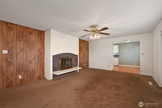 unfurnished living room featuring carpet floors, a textured ceiling, wood walls, and a fireplace