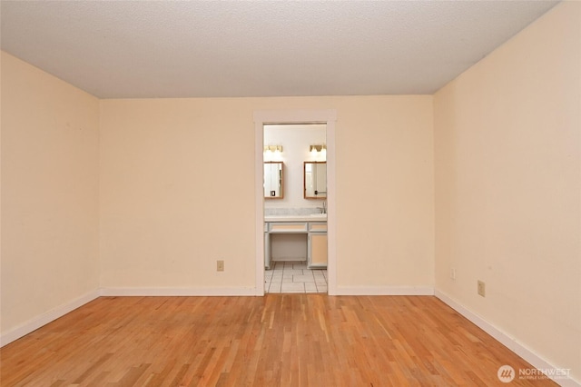 unfurnished bedroom featuring light wood finished floors, a textured ceiling, and baseboards