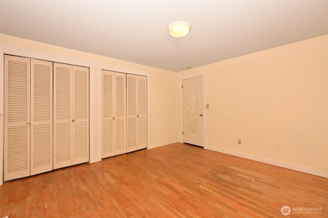 unfurnished bedroom featuring two closets, light wood-type flooring, and baseboards