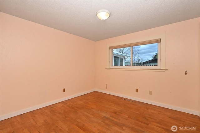 unfurnished room featuring a textured ceiling, wood finished floors, visible vents, and baseboards