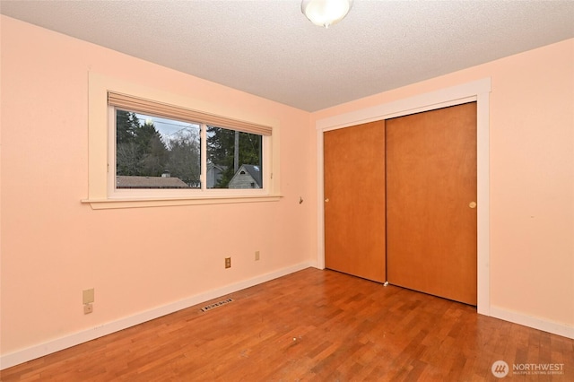 unfurnished bedroom featuring baseboards, wood finished floors, visible vents, and a textured ceiling