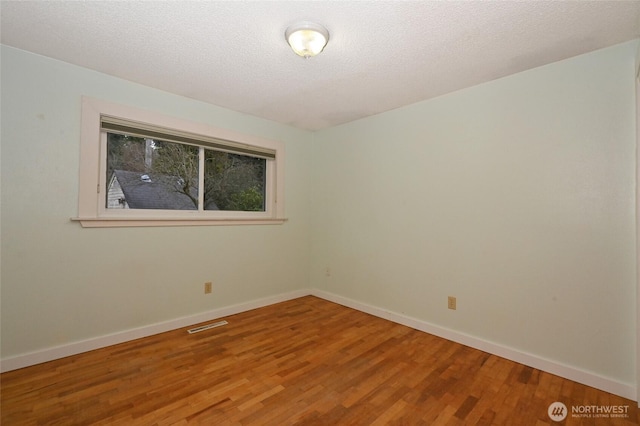 spare room with visible vents, baseboards, a textured ceiling, and wood finished floors