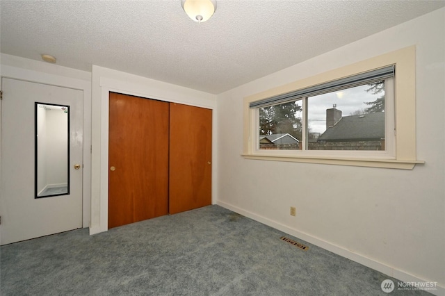 unfurnished bedroom with visible vents, a textured ceiling, a closet, carpet floors, and baseboards