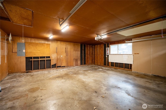 garage featuring electric panel, a garage door opener, and wood walls