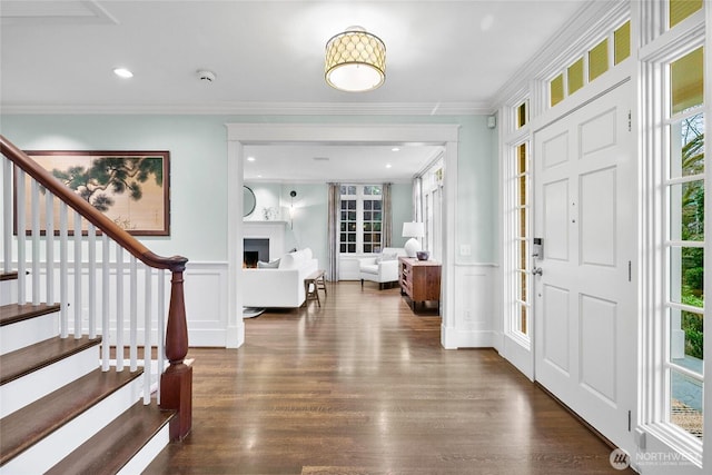 entryway with dark wood-style floors, stairway, a lit fireplace, crown molding, and a decorative wall