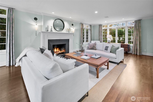 living room with recessed lighting, ornamental molding, wood finished floors, a warm lit fireplace, and baseboards