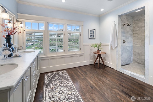 bathroom featuring a tile shower, wood finished floors, a sink, and crown molding