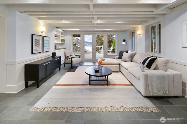 living area featuring built in features, beam ceiling, a wainscoted wall, french doors, and a decorative wall