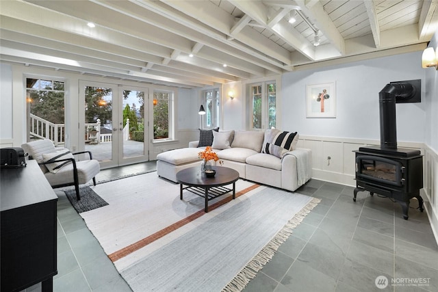 living area featuring tile patterned flooring, a wainscoted wall, french doors, beam ceiling, and a wood stove