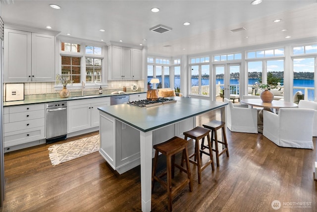 kitchen featuring dark countertops, open floor plan, a water view, stainless steel appliances, and white cabinetry