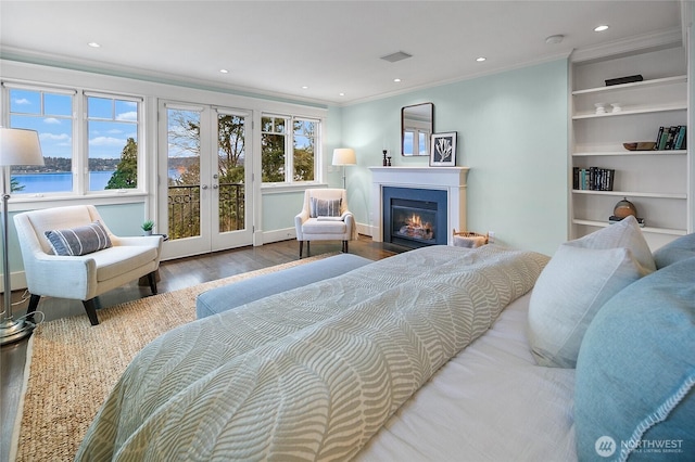 bedroom featuring a glass covered fireplace, ornamental molding, wood finished floors, a water view, and french doors