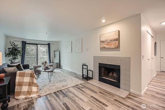 living room featuring baseboards, a tiled fireplace, and wood finished floors