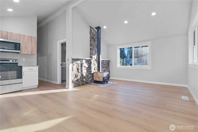 kitchen with open floor plan, light countertops, appliances with stainless steel finishes, light brown cabinetry, and a wood stove