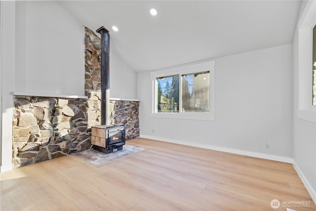 unfurnished living room with a wood stove, light wood-style floors, baseboards, and vaulted ceiling