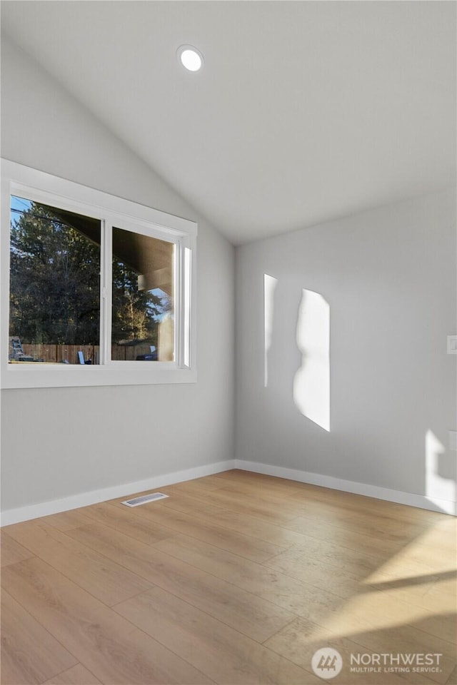 unfurnished room featuring vaulted ceiling, wood finished floors, visible vents, and baseboards