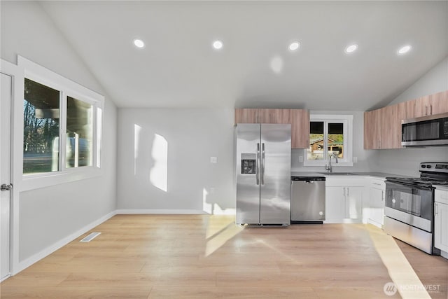 kitchen featuring white cabinets, stainless steel appliances, a sink, and lofted ceiling