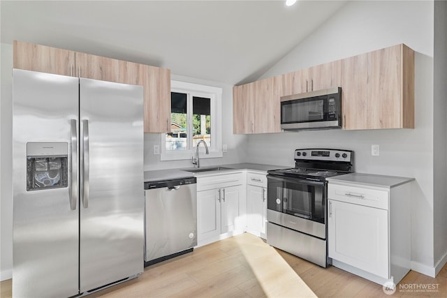 kitchen featuring light wood finished floors, appliances with stainless steel finishes, vaulted ceiling, light countertops, and a sink