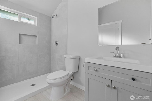 bathroom featuring tiled shower, vanity, toilet, and baseboards