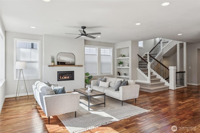 living area featuring stairs, baseboards, hardwood / wood-style floors, and a glass covered fireplace