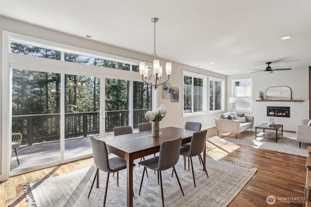 dining space featuring recessed lighting, visible vents, a glass covered fireplace, wood finished floors, and ceiling fan with notable chandelier