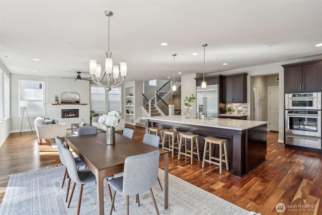 dining area with a lit fireplace, dark wood-type flooring, stairway, and recessed lighting