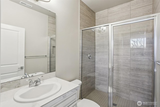 full bathroom featuring toilet, a stall shower, vanity, and visible vents