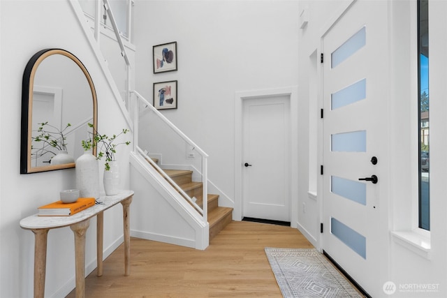 entryway with light wood-type flooring, baseboards, stairway, and a towering ceiling