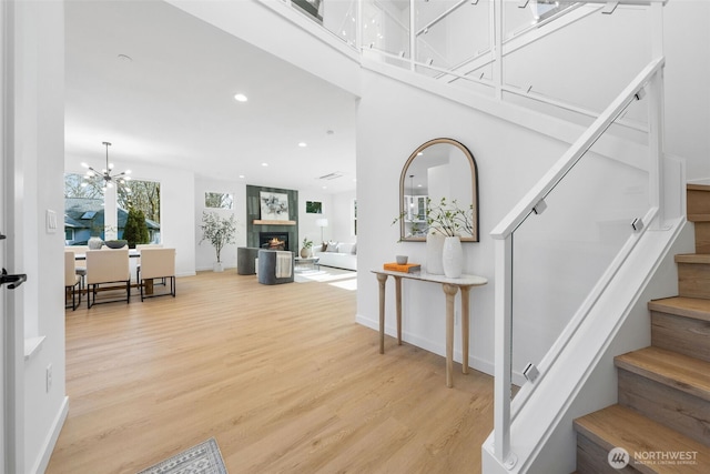 entrance foyer featuring baseboards, a lit fireplace, stairs, light wood-style floors, and recessed lighting