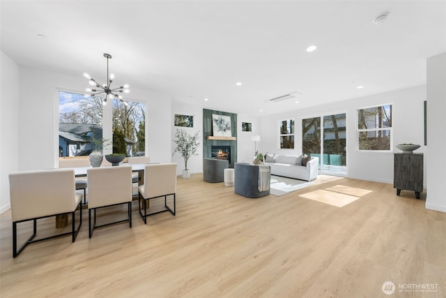 dining area with light wood-style flooring, recessed lighting, baseboards, a glass covered fireplace, and an inviting chandelier