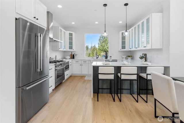 kitchen with a breakfast bar area, high end appliances, light wood-type flooring, a peninsula, and wall chimney exhaust hood