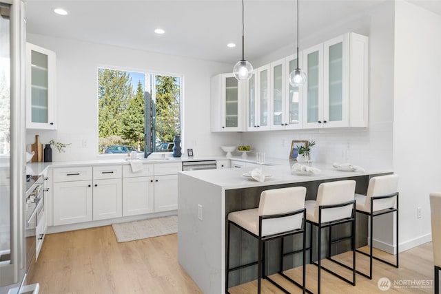 kitchen with white cabinets, light wood finished floors, a kitchen breakfast bar, and backsplash