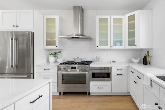 kitchen with appliances with stainless steel finishes, light wood-style floors, wall chimney range hood, and decorative backsplash