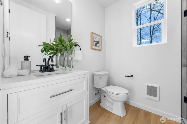 bathroom featuring heating unit, toilet, vanity, wood finished floors, and baseboards