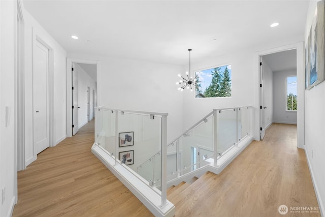 hall featuring baseboards, light wood-style flooring, an upstairs landing, a notable chandelier, and recessed lighting