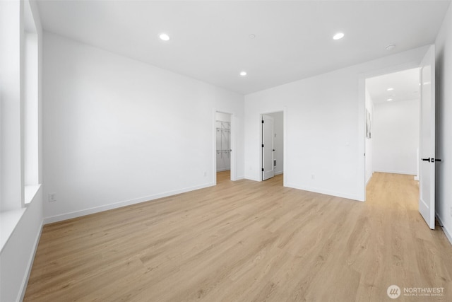 unfurnished bedroom with light wood finished floors, a spacious closet, baseboards, and recessed lighting