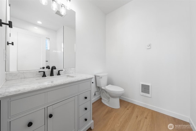 bathroom with visible vents, toilet, vanity, wood finished floors, and baseboards