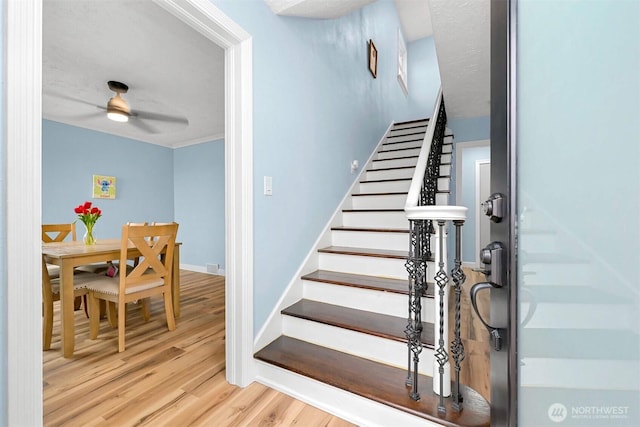 stairs with baseboards, wood finished floors, ceiling fan, and ornamental molding