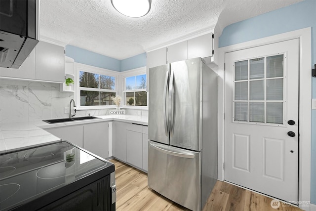 kitchen featuring black / electric stove, freestanding refrigerator, light wood-style floors, and a sink