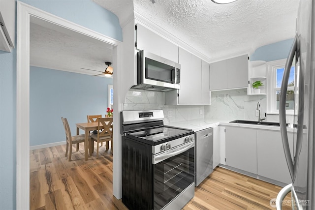 kitchen with a ceiling fan, open shelves, a sink, light wood-style floors, and appliances with stainless steel finishes