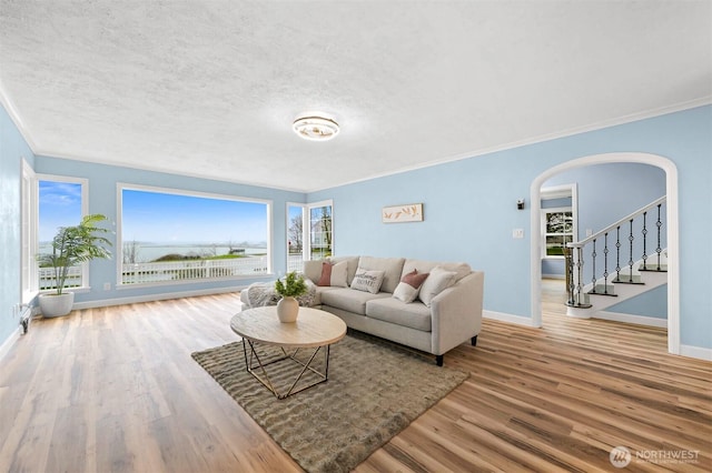 living area with a textured ceiling, wood finished floors, arched walkways, and baseboards