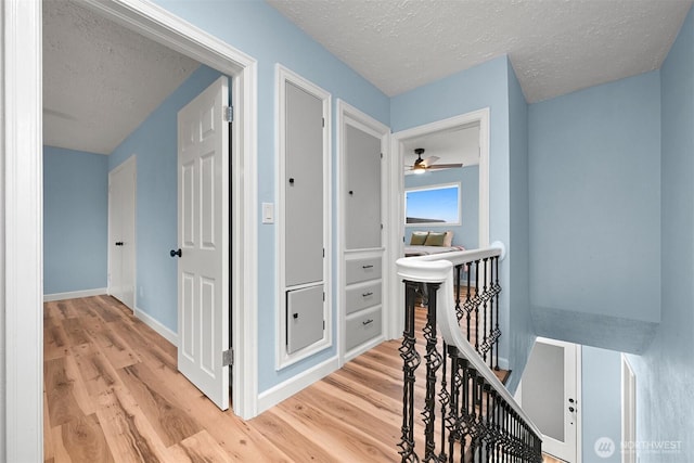 hallway featuring a textured ceiling, an upstairs landing, light wood-type flooring, and baseboards