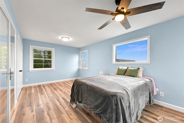 bedroom with multiple windows, baseboards, light wood-style floors, and ceiling fan