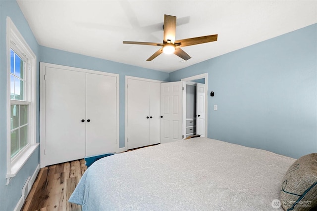 bedroom with visible vents, ceiling fan, baseboards, multiple closets, and wood finished floors