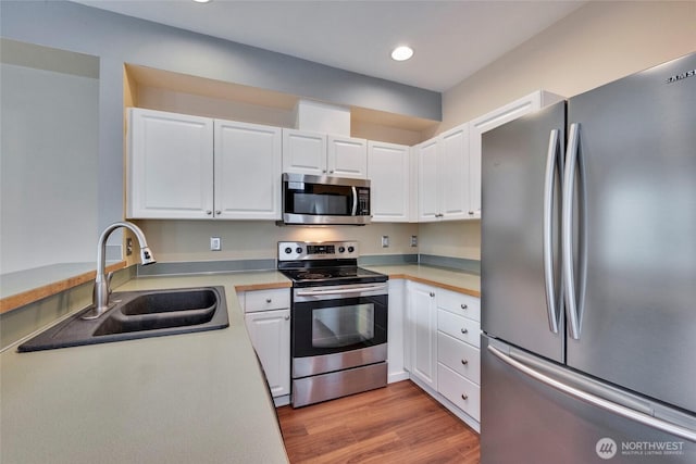 kitchen with light wood finished floors, appliances with stainless steel finishes, a sink, and white cabinetry