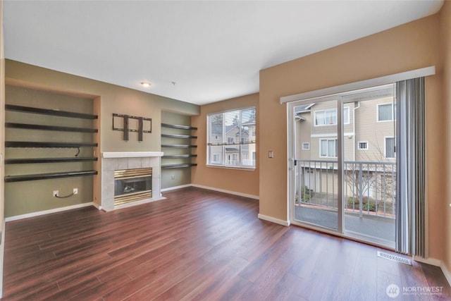 unfurnished living room with built in features, visible vents, baseboards, dark wood-style flooring, and a fireplace