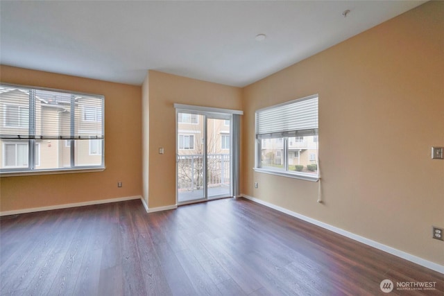 unfurnished room with a wealth of natural light, dark wood finished floors, and baseboards