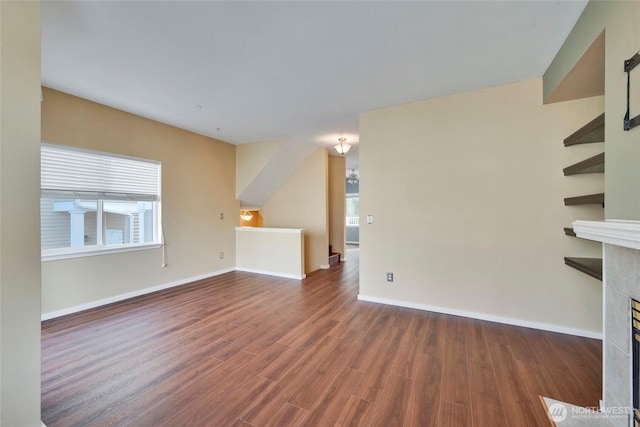 unfurnished living room featuring baseboards, a tiled fireplace, and wood finished floors