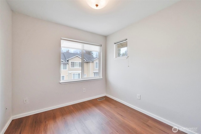 spare room with dark wood-style floors, visible vents, and baseboards